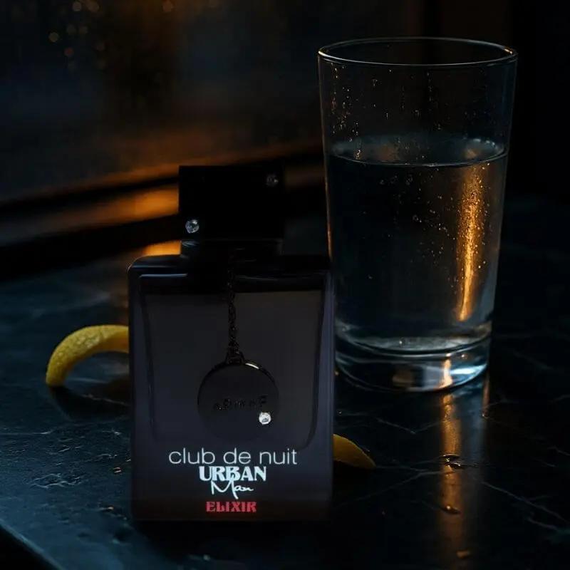 Parfum Armaf Club de Nuit Urban Man Elixir en flacon noir, posé sur une table sombre à côté d’un verre d’eau et d’un zeste de citron