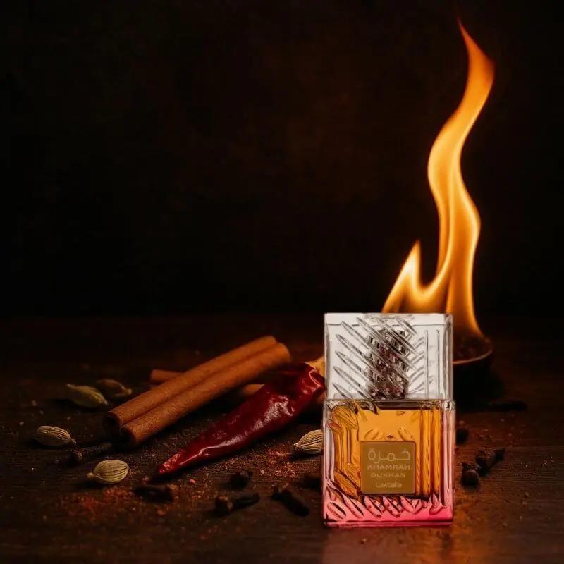 Parfum Khamrah Qahwa de Lattafa en flacon transparent et doré, posé sur une table avec des épices, un piment rouge et une flamme en arrière-plan
